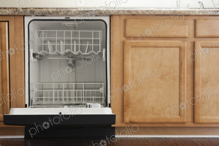 An open dishwasher in a kitchen with wooden fitted units.