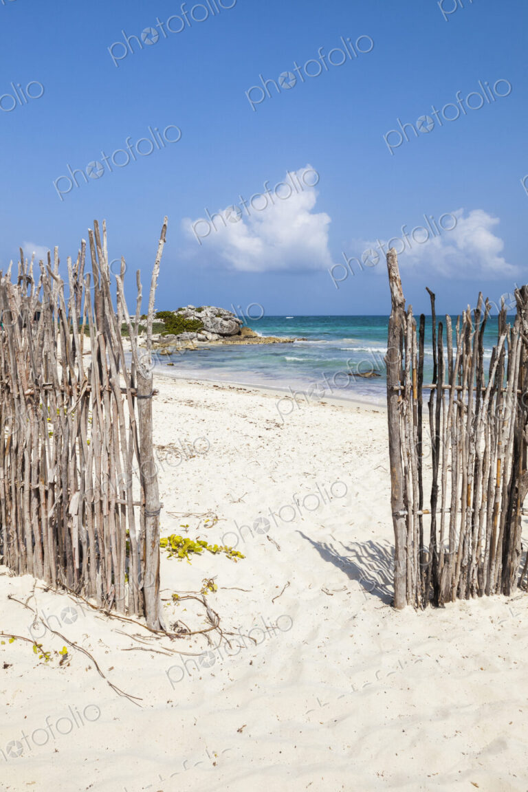 An opening in the fence onto a white sand beach