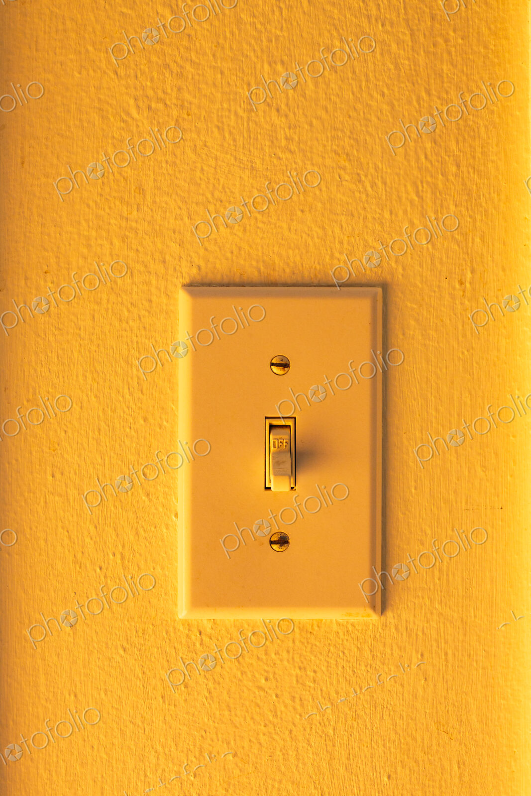 An orange wall and an orange rocker electric light switch,
