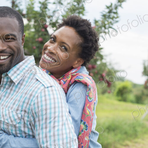 An organic apple tree orchard. A couple hugging and smiling at the camera.