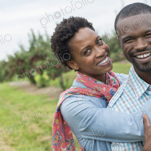 An organic apple tree orchard. A couple hugging and smiling at the camera.
