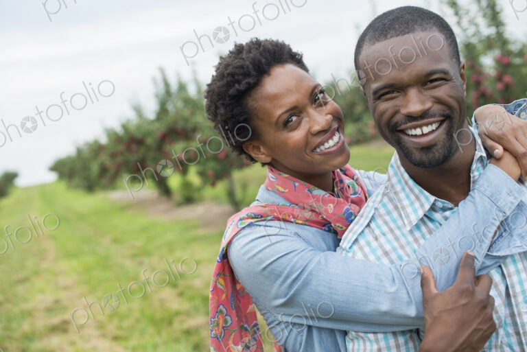 An organic apple tree orchard. A couple hugging and smiling at the camera.