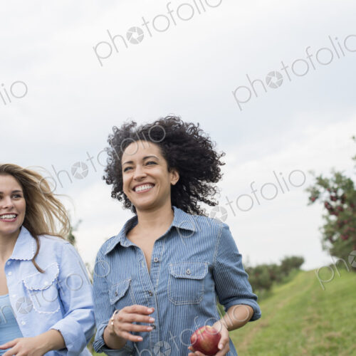 An organic apple tree orchard. Two women carrying apples in their hands.
