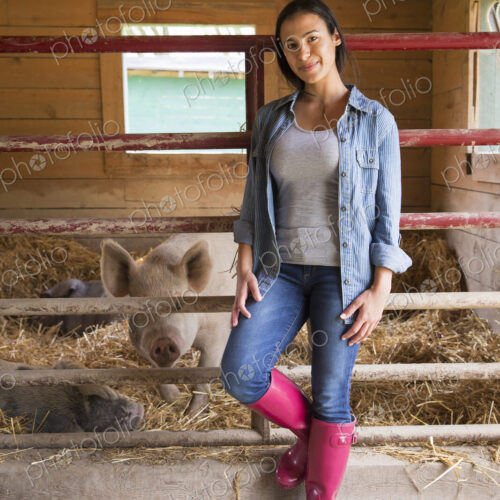 An organic farm in the Catskills. A woman beside a pig in a pen, standing in deep straw.
