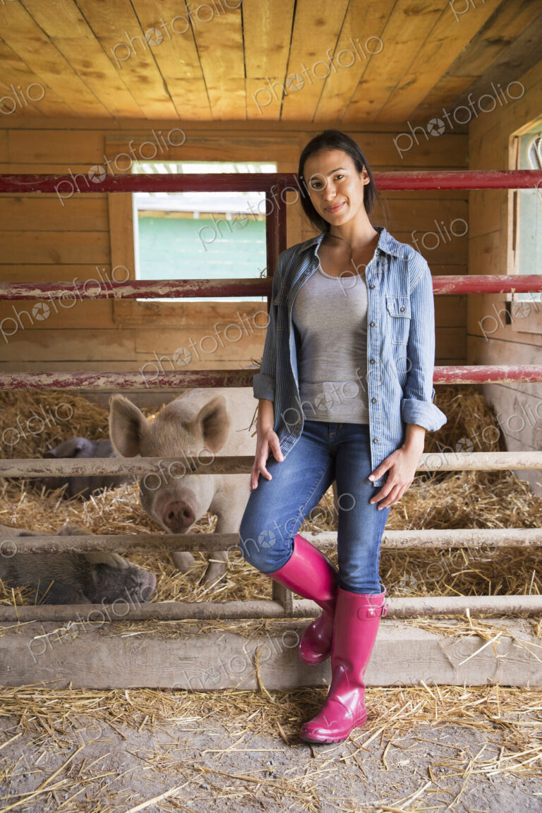 An organic farm in the Catskills. A woman beside a pig in a pen, standing in deep straw.