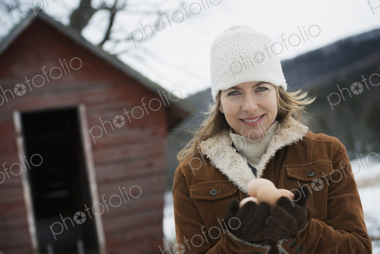 An organic farm in upstate New York, in winter. A woman holding a clutch of hen's eggs…