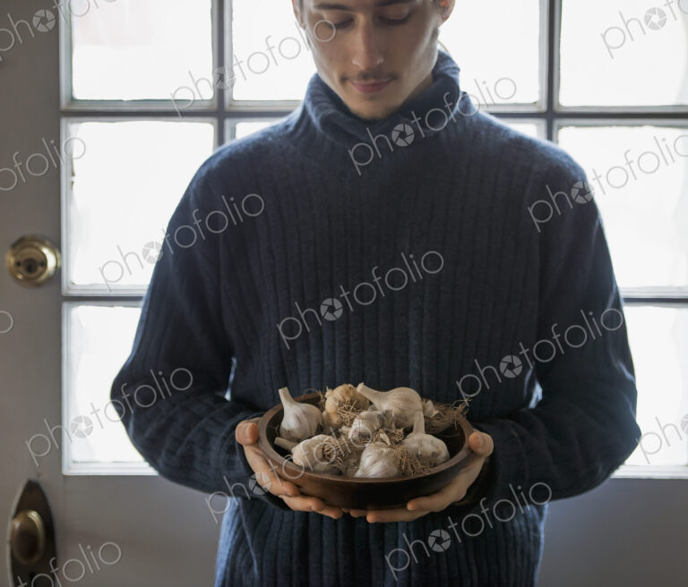 An organic farm in winter in New York State, USA. A young man holding a bow of garlic…