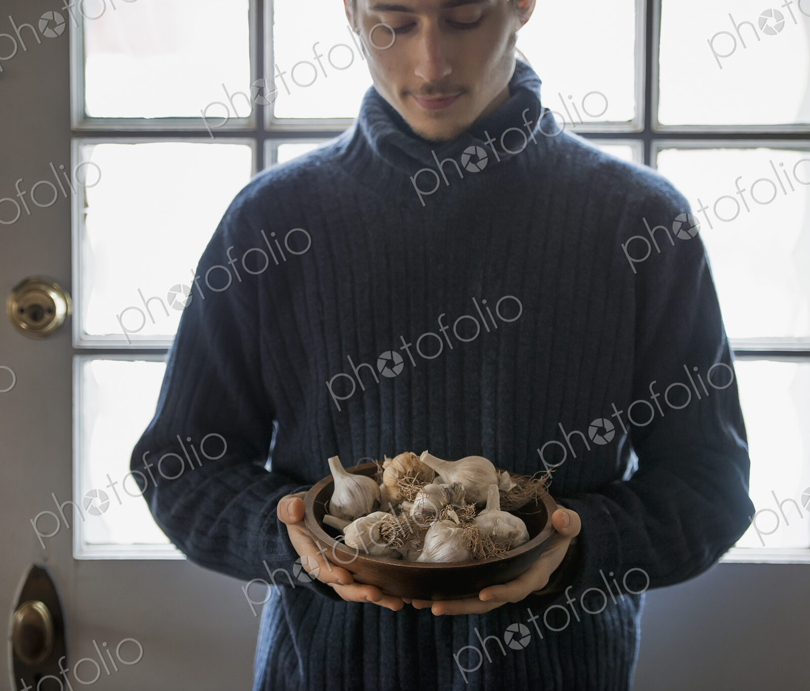An organic farm in winter in New York State, USA. A young man holding a bow of garlic…