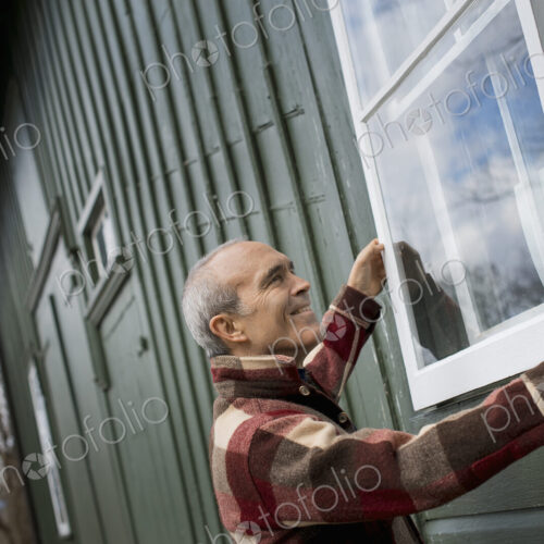 An organic farm in winter. Maintenance. A man holding a a storm window panel against… An organic farm in winter. Maintenance. A man holding a a storm window panel against…