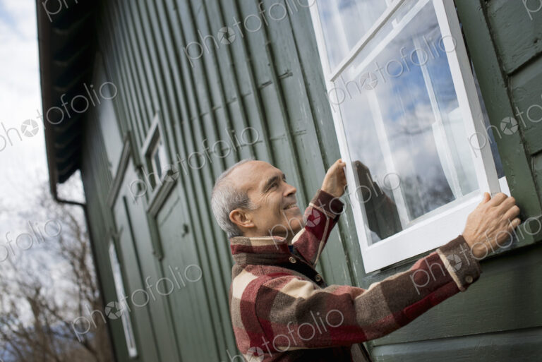 An organic farm in winter. Maintenance. A man holding a a storm window panel against…