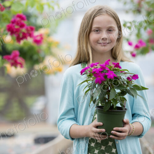 An organic flower plant nursery. A young girl holding a flowering plant. An organic flower plant nursery. A young girl holding a flowering plant.