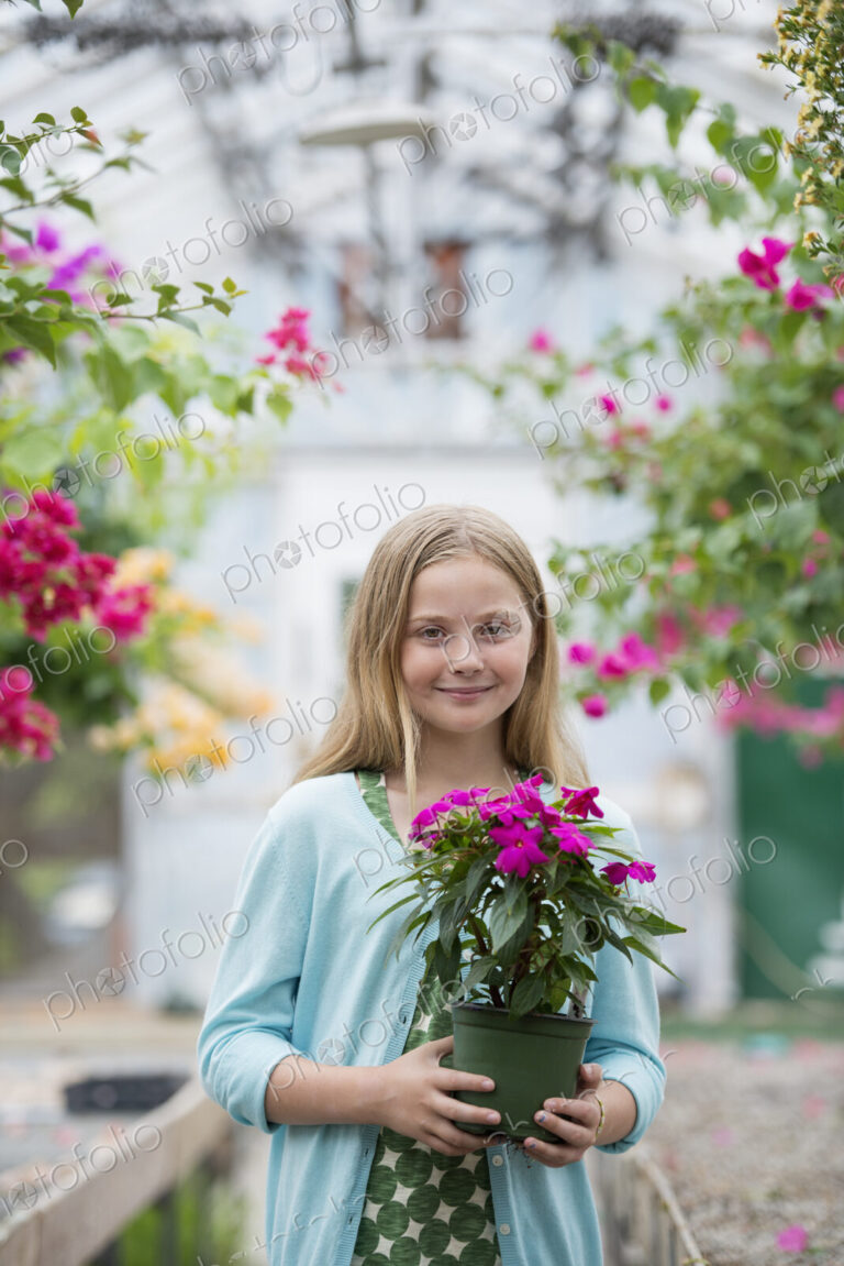 An organic flower plant nursery. A young girl holding a flowering plant.