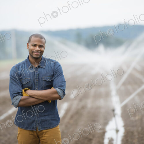 An organic vegetable farm, with water sprinklers irrigating the fields. A man in… An organic vegetable farm, with water sprinklers irrigating the fields. A man in…