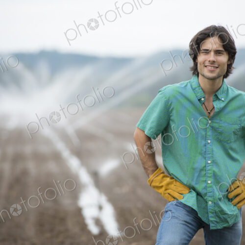 An organic vegetable farm, with water sprinklers irrigating the fields. A man in…