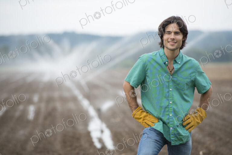 An organic vegetable farm, with water sprinklers irrigating the fields. A man in…