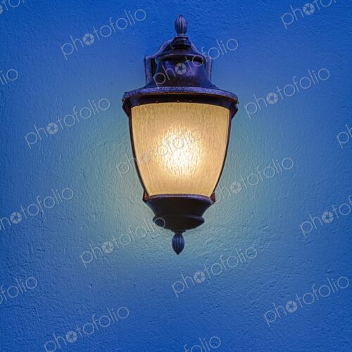 An ornate streetlight glows warmly against a vivid blue wall in Old San Juan, Puerto… An ornate streetlight glows warmly against a vivid blue wall in Old San Juan, Puerto…