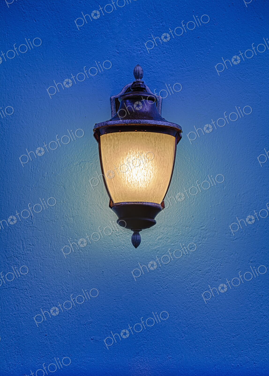 An ornate streetlight glows warmly against a vivid blue wall in Old San Juan, Puerto…