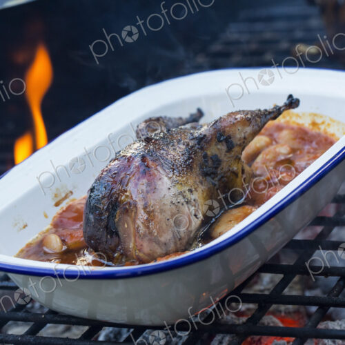 An outdoor cookout, a game bird in a pan braising with vegetables. An outdoor cookout, a game bird in a pan braising with vegetables.