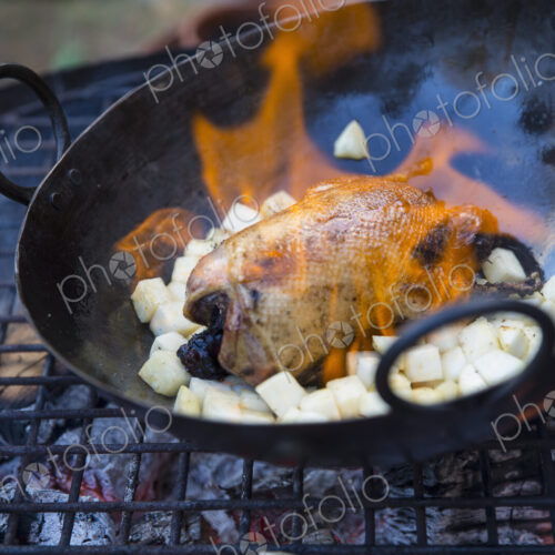 An outdoor cookout, a game bird in a pan with flame licking around the carcass,… An outdoor cookout, a game bird in a pan with flame licking around the carcass,…
