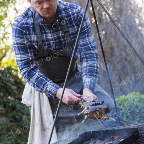 An outdoor cookout, a man lifted game birds off the griddle of an open fire. An outdoor cookout, a man lifted game birds off the griddle of an open fire.