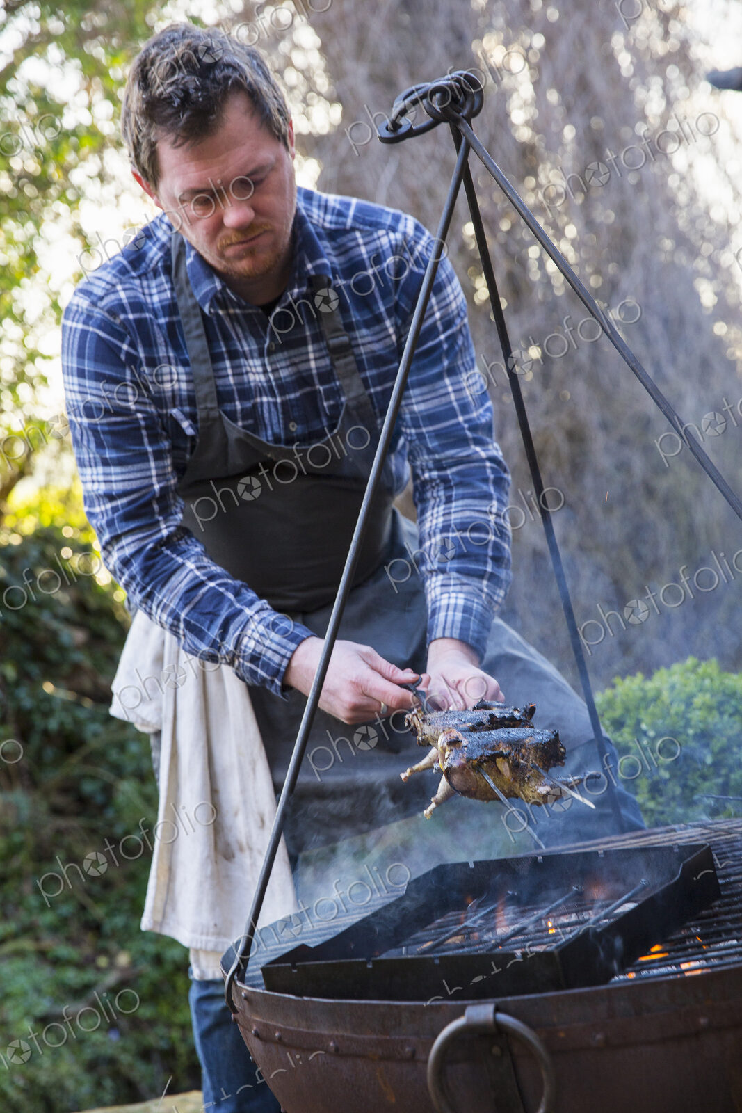 An outdoor cookout, a man lifted game birds off the griddle of an open fire.