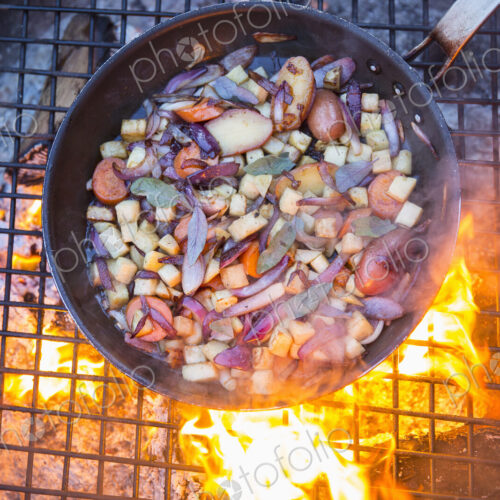 An outdoor cookout, game birds in a pan above a glowing fire. An outdoor cookout, game birds in a pan above a glowing fire.