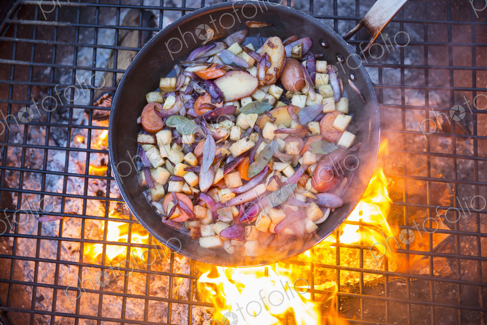 An outdoor cookout, game birds in a pan above a glowing fire.