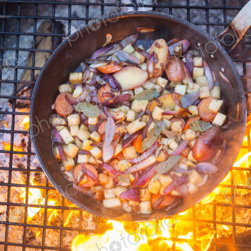 An outdoor cookout, game birds in a pan above a glowing fire. An outdoor cookout, game birds in a pan above a glowing fire.