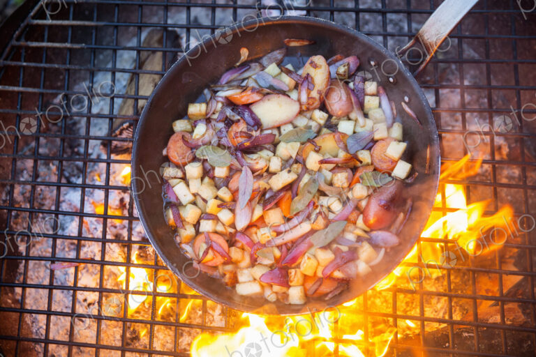 An outdoor cookout, game birds in a pan above a glowing fire.