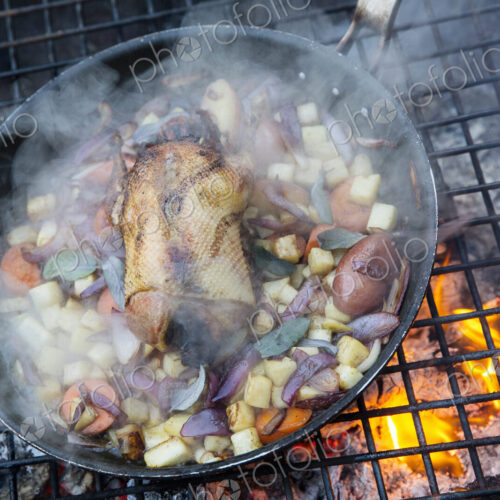 An outdoor cookout, game birds in a pan above a glowing fire. An outdoor cookout, game birds in a pan above a glowing fire.