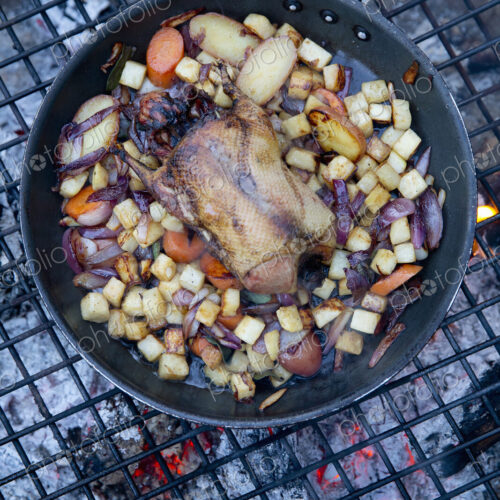 An outdoor cookout, game birds in a pan above a glowing fire. An outdoor cookout, game birds in a pan above a glowing fire.