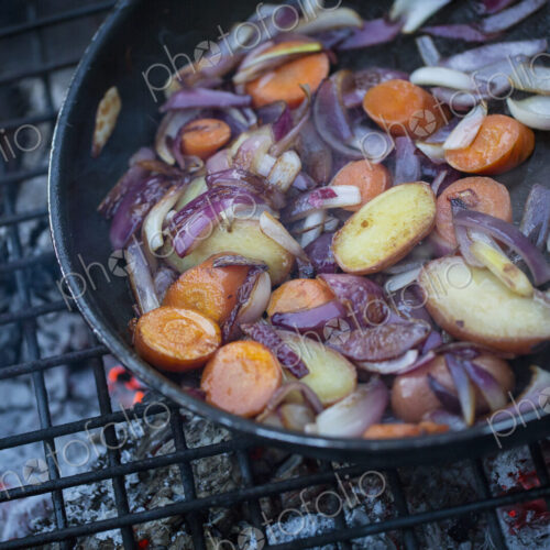 An outdoor cookout, vegetables in a frying pan above a glowing fire. An outdoor cookout, vegetables in a frying pan above a glowing fire.