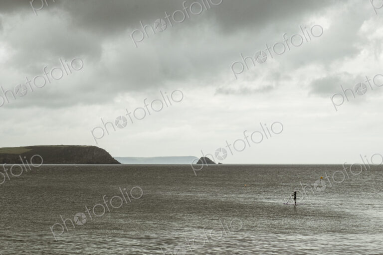 An overcast day with clouds, a view across a calm sea, to distant headlands and an…