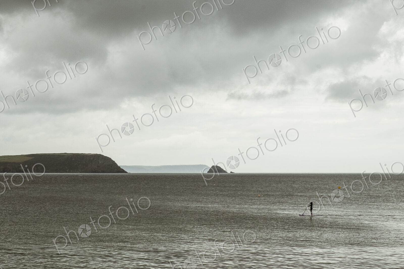 An overcast day with clouds, a view across a calm sea, to distant headlands and an…