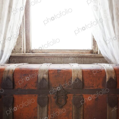 Antique steamer trunk sits beneath a bright window with lace curtains. Warm sunlight…