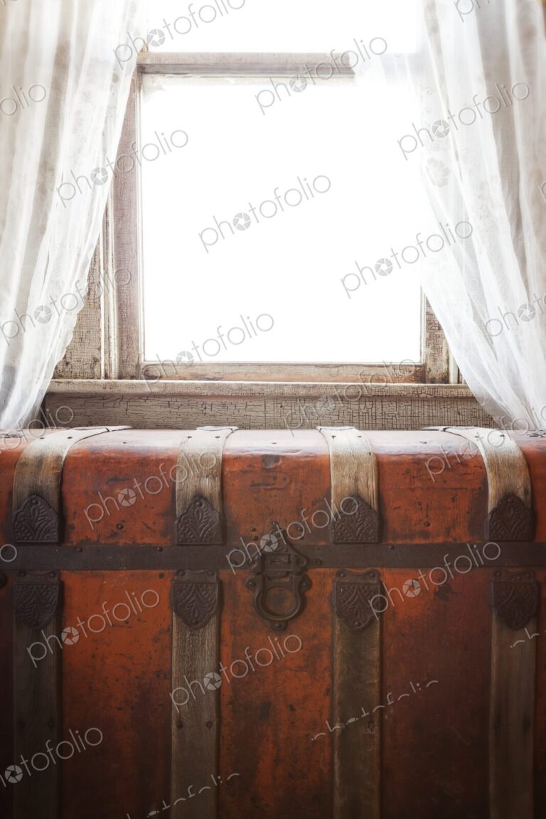 Antique steamer trunk sits beneath a bright window with lace curtains. Warm sunlight…