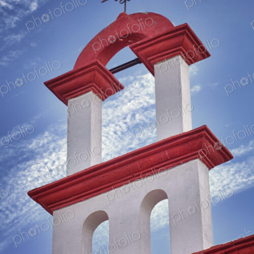 Architectural detail, red and white paint and iron cross on a church rooftop in Cancun.