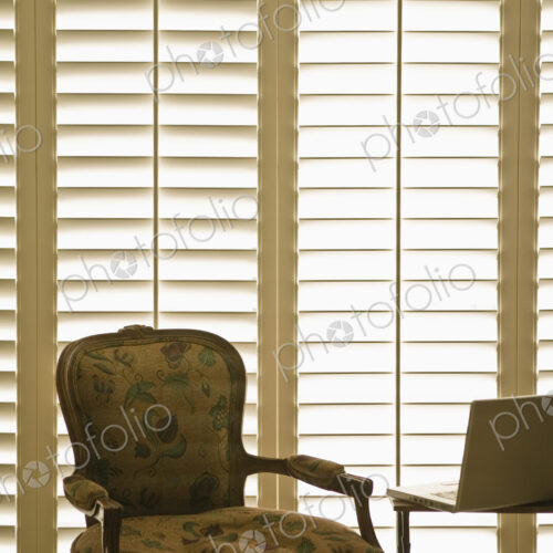 Armchair and laptop in front of domestic wooden window shutters.