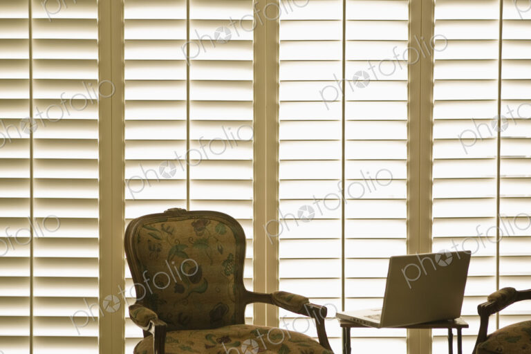 Armchair and laptop in front of domestic wooden window shutters.