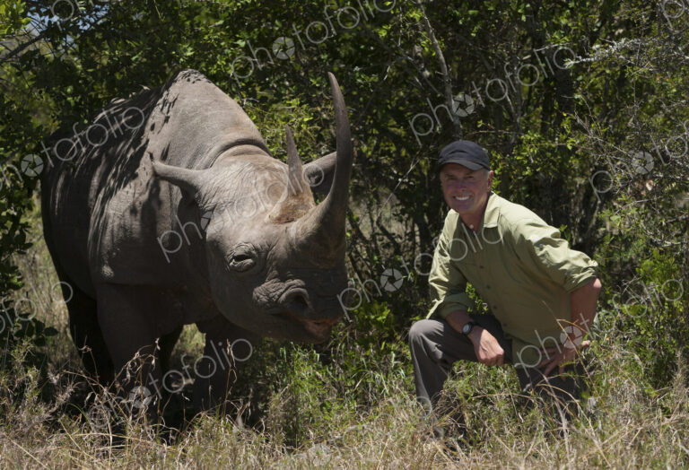 Art Wolfe, photographer kneeling next to a white rhinoceros in Kenya.