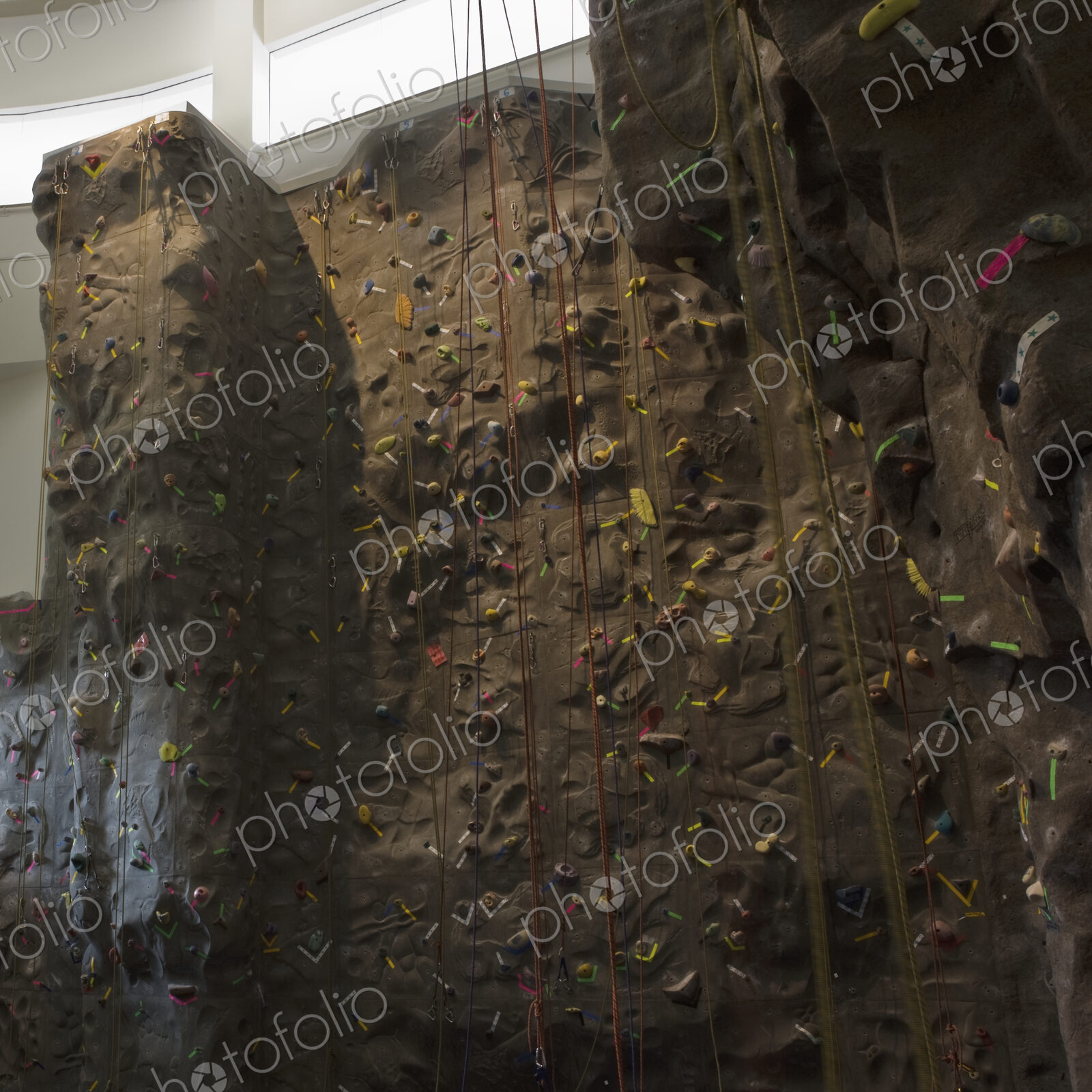 Artificial climbing wall with ropes in indoor climbing centre.