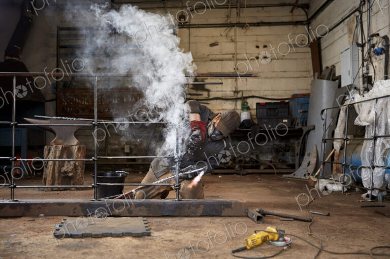Artisan metalworker at work in a workshop working, soldering a metal fence.