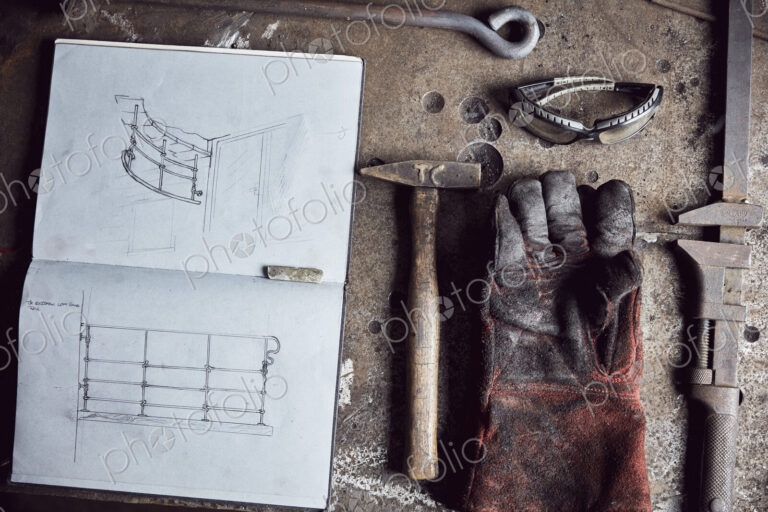 Artisan metalworker's tools, sketches in a notebook and a glove