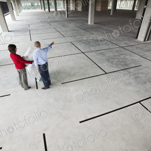 Asian architect with caucasian woman planning workspaces in a new raw office location