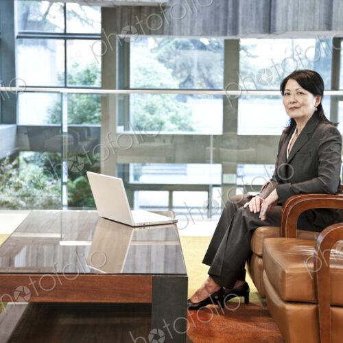 Asian business woman sitting on a couch in the lobby area of a convention center.