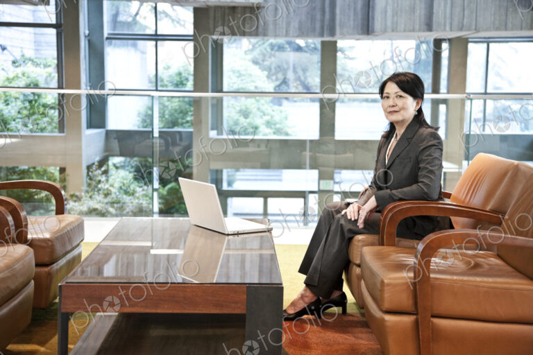 Asian business woman sitting on a couch in the lobby area of a convention center.