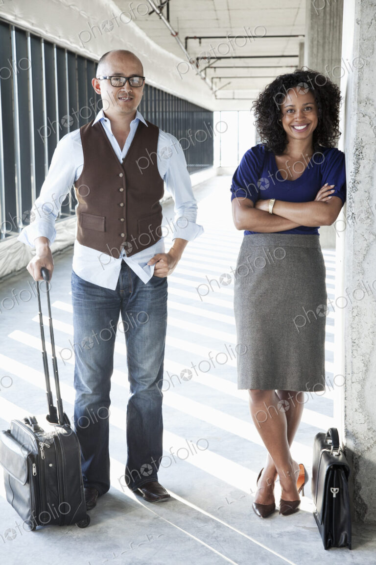Asian businessman and black businesswoman in a large empty office space lit by the…