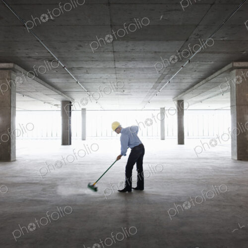 Asian businessman cleaning up with a broom in a large empty raw office space. Asian businessman cleaning up with a broom in a large empty raw office space.