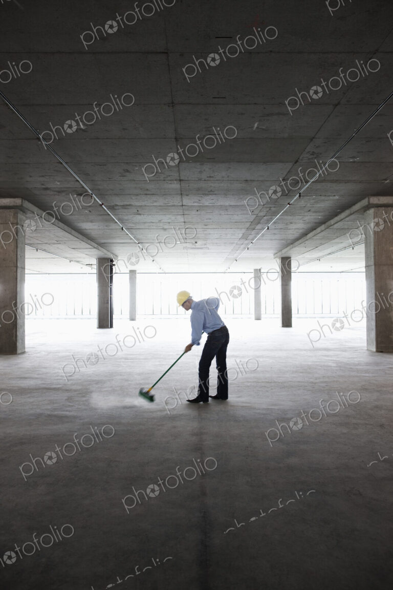Asian businessman cleaning up with a broom in a large empty raw office space.