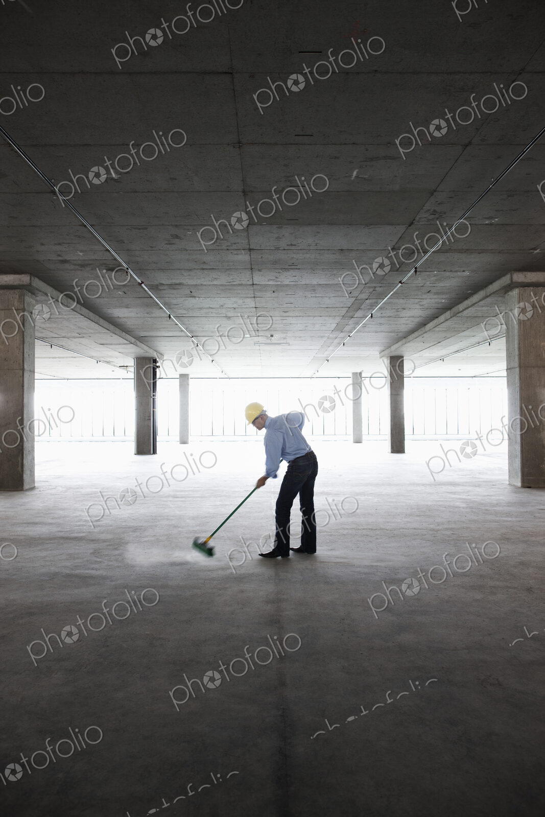 Asian businessman cleaning up with a broom in a large empty raw office space.